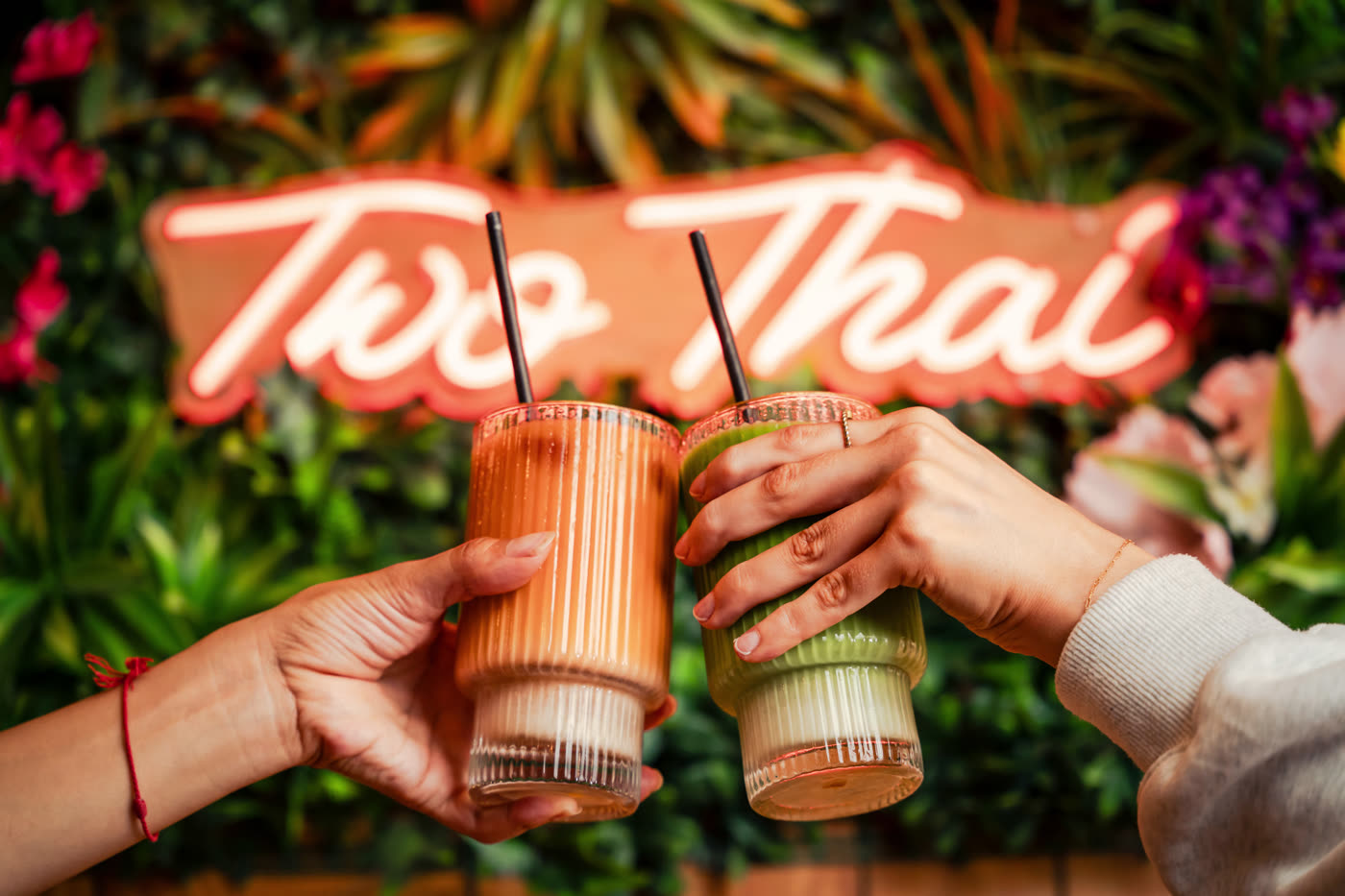 Two Thai iced teas held up in front of the neon Two Thai sign.