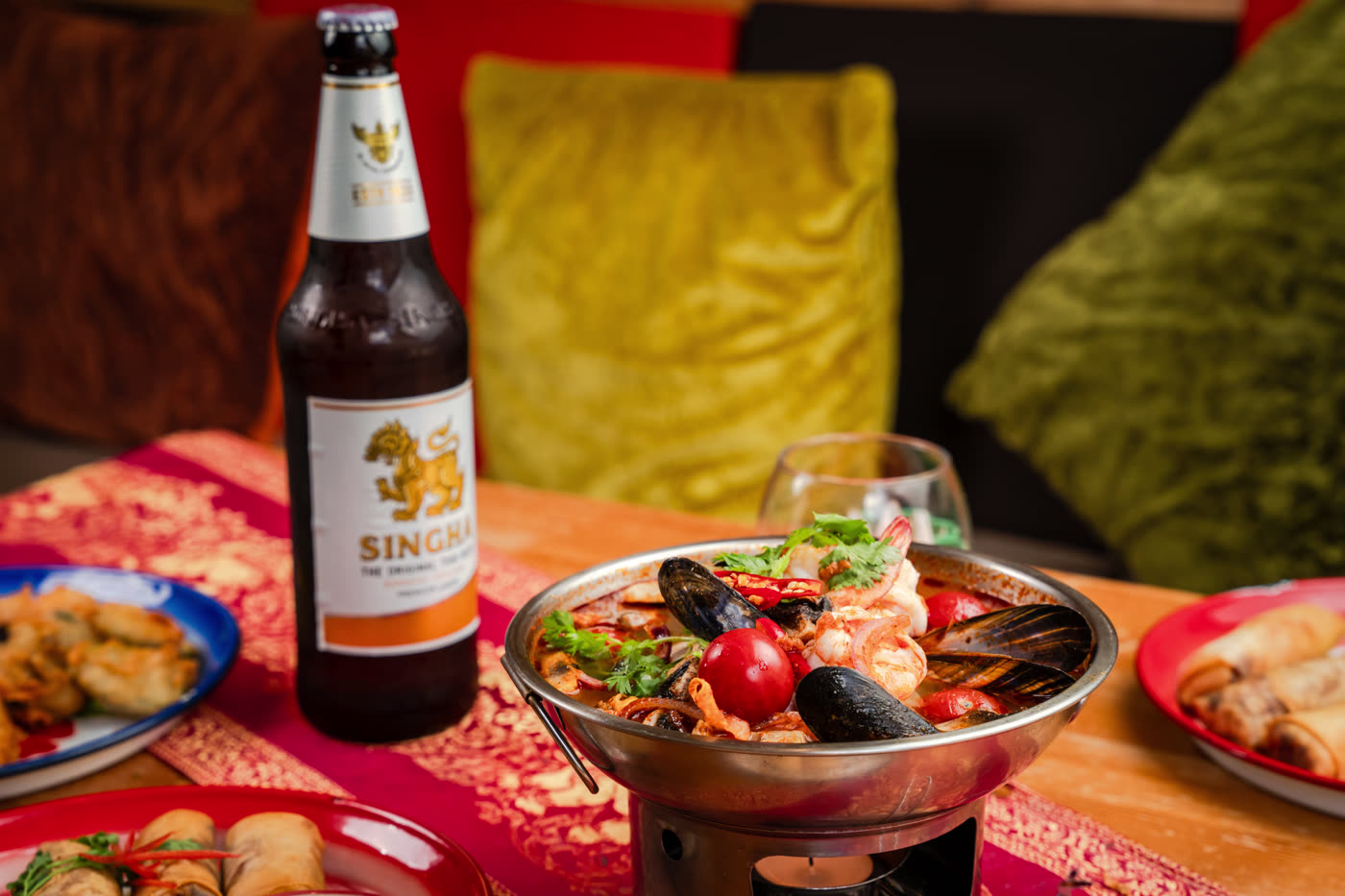 A seafood hot pot bubbling over its burner beside a bottle of Singha.
