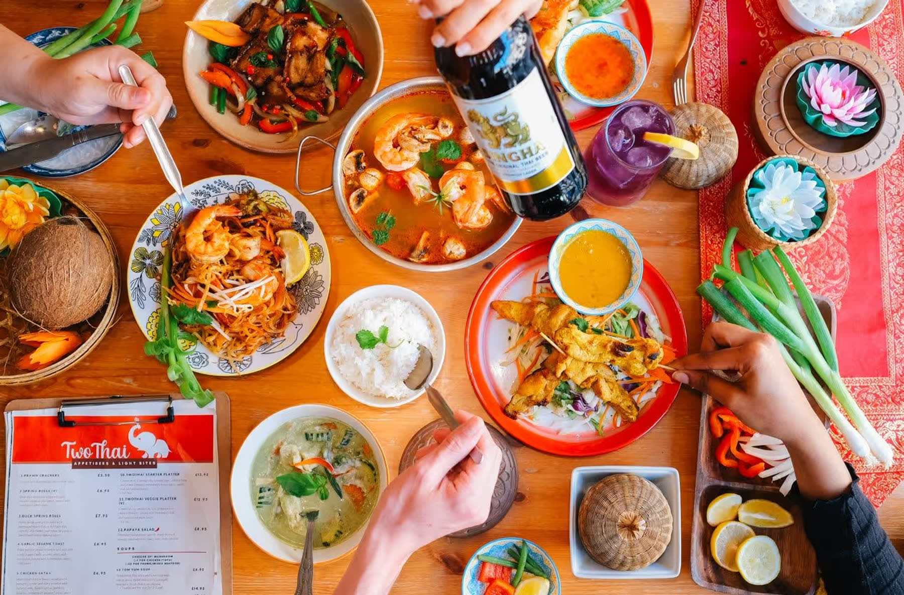 A shared table laid with pad thai, curries, satay, rice and a bottle of Singha.